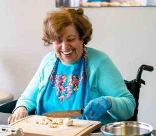 Individual participating in ARBI's cooking program, chopping mushrooms on an adaptive cutting board.